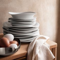 a stack of plates and bowls with eggs in them sitting on a table next to a white towel