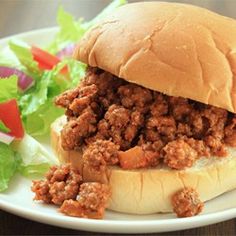 a sloppy joe sandwich with lettuce and tomato salad on the side is ready to be eaten