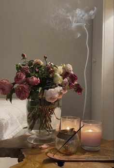 a glass vase filled with flowers on top of a wooden table next to two candles