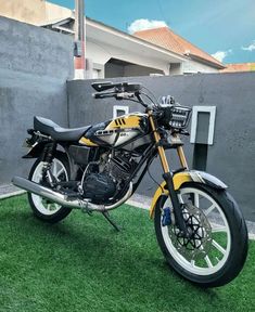 a yellow and black motorcycle parked on top of a green grass covered field next to a building