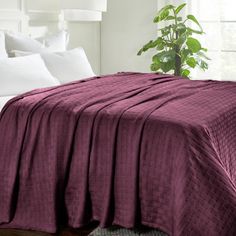 a bed covered in a purple blanket next to a white headboard with pillows and a potted plant