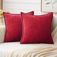 two red pillows sitting on top of a white couch next to a vase with flowers