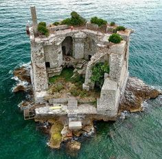 an old stone building sitting on top of the ocean with plants growing out of it