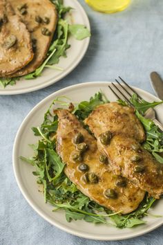 two white plates topped with meat and greens