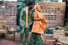 a man and woman dressed in traditional african clothing standing next to each other on a brick patio