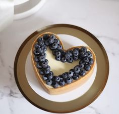 a heart shaped cake with blueberries on it sitting on a plate next to a cup