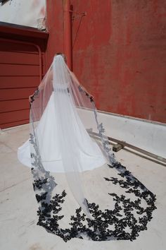 a bride's veil is covered with black flowers on her wedding day in front of a red building