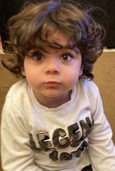 a little boy sitting on the floor with his hands in his pockets and looking at the camera