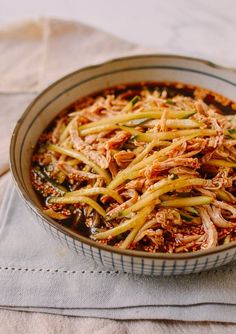 a bowl filled with meat and vegetables on top of a cloth covered placemat next to a napkin