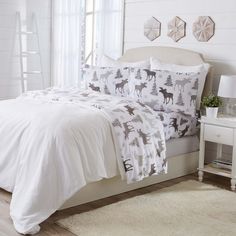 a white bed with deer and pine trees printed on the comforter, along with two night stands