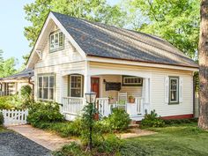 a small white house in the middle of some trees and grass with a brick walkway leading up to it