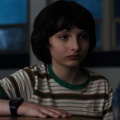 a young boy sitting at a table with his hand on the top of his arm