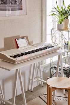 an electronic keyboard sitting on top of a white table next to a chair and potted plant