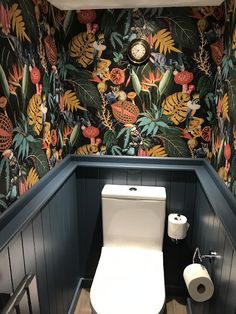 a toilet in the corner of a bathroom with floral wallpaper and wooden flooring