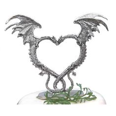 a heart shaped sculpture with wings on top of a white surface and greenery in the foreground