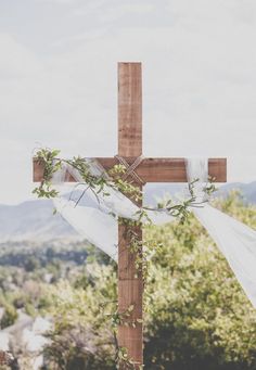 a wooden cross decorated with greenery on top of a hill next to a forest