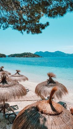 many straw umbrellas and chairs are on the beach near the blue water with mountains in the distance