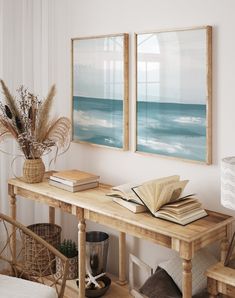 two paintings hanging on the wall above a wooden table with books and plants in front of it