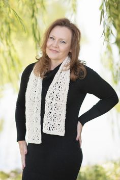 a woman standing in front of a tree wearing a white knitted scarf and black top