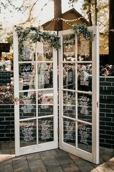 an open glass door with chalkboard menus on the side and greenery around it