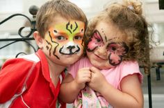 two young children with face paint on their faces, one is hugging the other's chest