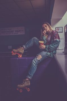 a woman sitting on top of a purple counter next to a cup and skateboard