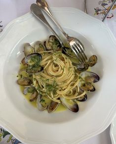 a white plate topped with pasta and clams on top of a table next to silverware