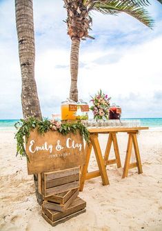 a wooden sign sitting next to a palm tree on top of a sandy beach near the ocean