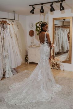 a woman standing in front of a mirror wearing a wedding dress with an open back