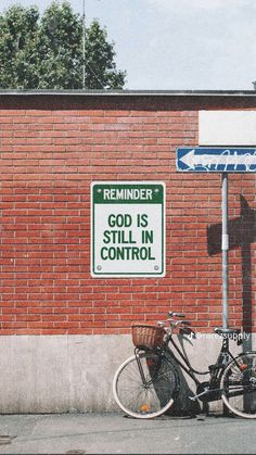 a bicycle parked next to a street sign on the side of a brick building with a green and white sign that reads reminder god is still in control