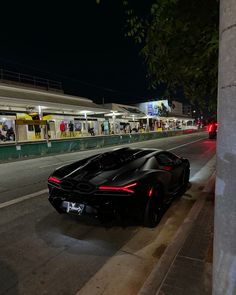 a black sports car is parked on the side of the road at night with people walking by