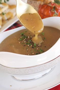 a spoon full of gravy being lifted from a white bowl filled with soup