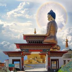 a large buddha statue sitting in front of a tall building with a rainbow behind it