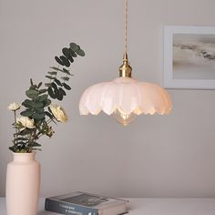 a white vase with flowers and a light hanging from it's side next to a book on a table