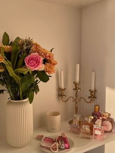 a white vase filled with pink flowers next to candles and other items on a table