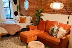 an orange couch sitting in front of a brick wall next to a bed with pillows on it