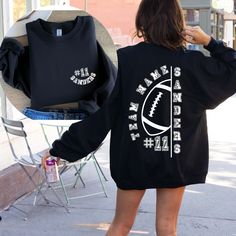 a woman is walking down the street wearing a black sweatshirt with white letters and a football on it