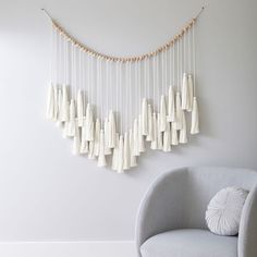 a chair sitting in front of a wall hanging with white tassels on it