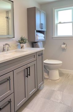 a white toilet sitting next to a sink in a bathroom under a window with a towel dispenser on it