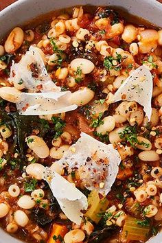 a white bowl filled with pasta and beans covered in parmesan cheese on top of a wooden table