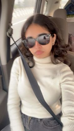 a woman sitting in the back seat of a car wearing sunglasses and holding onto a camera strap