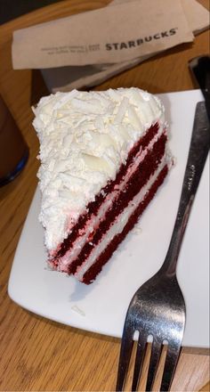 a piece of red velvet cake with white frosting on a plate next to a fork