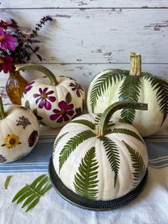 three painted pumpkins sitting on top of a table next to purple flowers and greenery