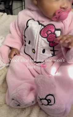 a baby in a pink hello kitty outfit is holding a pacifier to her mouth