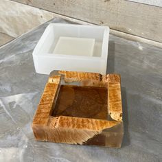 a square wooden box sitting on top of a table next to a white container filled with liquid