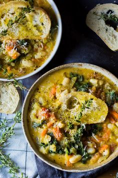 two bowls of vegetable soup with bread on the side and sprig of rosemary