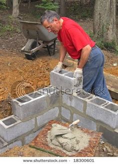 a man is building a brick wall in the yard with concrete blocks and cement mortar