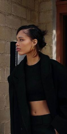 a woman standing next to a brick wall wearing a black jacket and cropped top