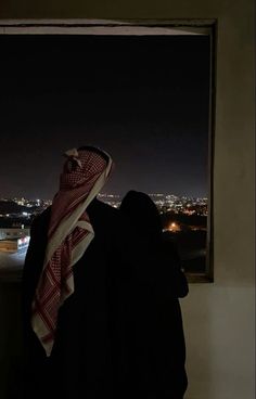 a man standing in front of a window looking out at the night cityscape