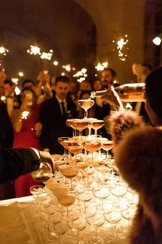 many people are holding wine glasses with sparklers in the air as they sit at a table full of champagne flutes